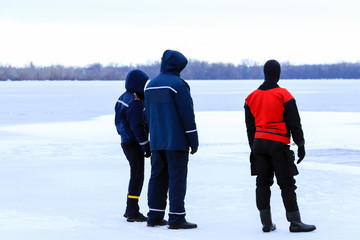 Rescuers in uniform and diving suit are on duty on the ice of a frozen river during winter fishing...
