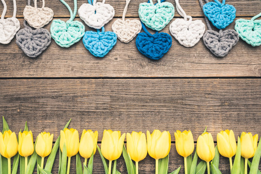 Beautiful yellow tulips arranged next to each other and crocheted colorful hearts. Flowers and hearts placed on an old wooden boards. Plants frame with copy, free space best for every occasion.