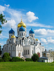 Transfiguration Cathedral at Nikolo Ugreshskiy Monastery old historical white church with blue gold domes on a spring summer day with blue cloudy sky, green grass, plants and trees