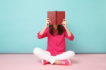 Full length portrait of smiling woman in rose shirt blouse, white pants sit on floor read book...