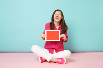 Full length portrait woman in rose shirt blouse, white pants sitting on floor hold tablet pc...