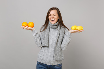 Laughing young woman in gray sweater, scarf with closed eyes hold lemons oranges isolated on grey background. Healthy fashion lifestyle people sincere emotions cold season concept. Mock up copy space.