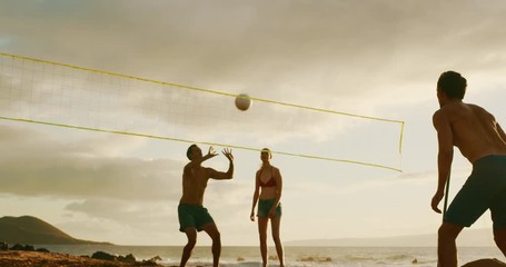 Group of friends playing beach volleyball at sunset, athletic man dives to save volleyball, slowmotion