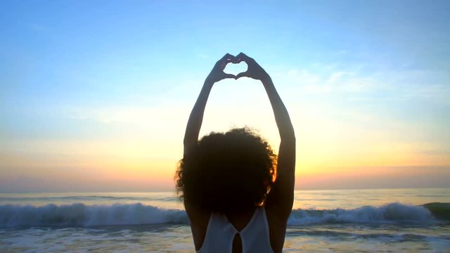 Happy young African American woman showing heart sign with hands at sunset
