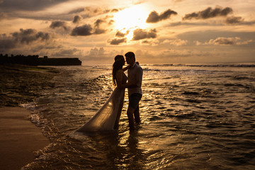 Fototapeta premium Bride and groom hug standing in the sea water on the beach at sunset
