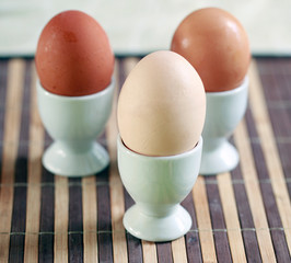 different colors eggs and white glass egg holders, on a brown mat: rustic breakfast