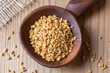 Fenugreek seeds on a wooden spoon on a table