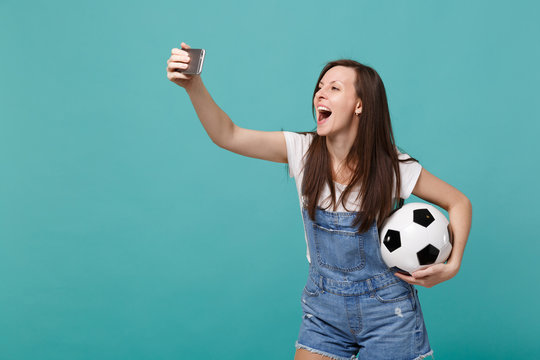 Cheerful young woman football fan with soccer ball doing selfie shot on mobile phone isolated on blue turquoise background. People emotions, sport family leisure lifestyle concept. Mock up copy space.