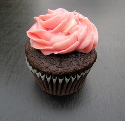 Chocolate cupcake with pink frosting over black background