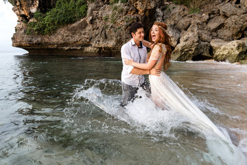 Bride and groom have fun frolicking in the sea water on the beach