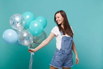 Portrait of smiling young woman in denim clothes looking aside, celebrating, holding colorful air...