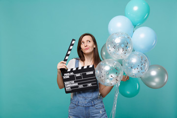 Puzzled woman looking up, holding classic black film making clapperboard, celebrating with colorful...
