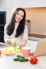 Obraz na płótnie Canvas Picture of happy asian girl with mug and laptop standing at table with vegetables and fruits