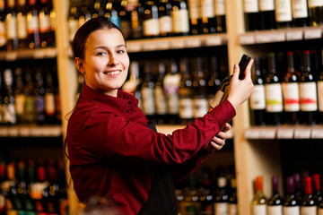 Picture of young woman with bottle in her hands in wine shop