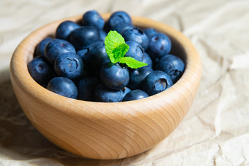 A wooden bowl full of blueberries with plain soft background decorated by fresh mint