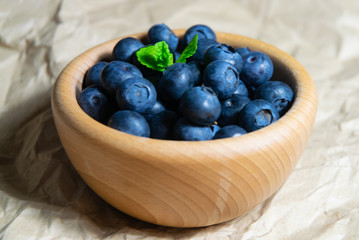A wooden bowl full of blueberries with plain soft background decorated by fresh mint
