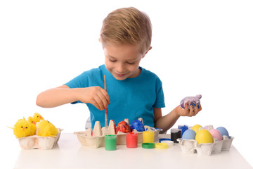 Fototapeta na wymiar The child is painting Easter eggs. The boy is sitting at a table with colorful paints, his hands are dirty. She is happy, preparing for Easter. White isolated.