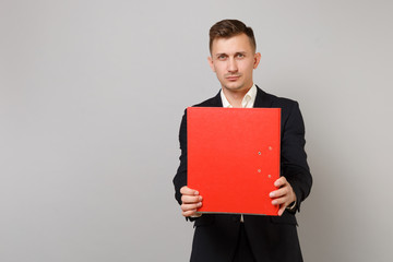 Attractive young business man in classic black suit, shirt holding red folder for papers document isolated on grey background in studio. Achievement career wealth business concept. Mock up copy space.