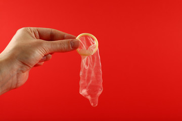 Close up man hand holding open condom over red