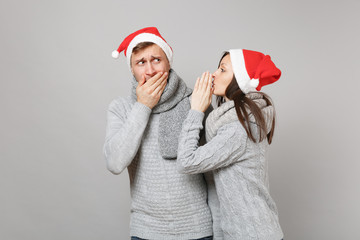 Merry fun couple girl guy in red Santa Christmas hat gray sweaters scarves isolated on grey wall...
