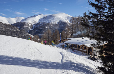 Brunnach Ski Resort, St. Oswald, Carinthia, Austria - January 20, 2019: A cabin next to the ski slope with skiers in front, mountains in the background