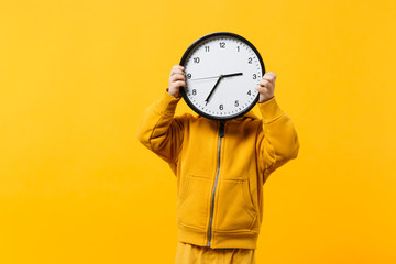 Little kid boy 3-4 years old wearing yellow clothes hold clock isolated on orange wall background,...