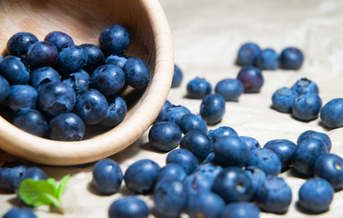 An isolated wooden bowl full of blueberries with plain soft background decorated by fresh mint and with a few blueberries around