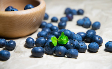 An isolated wooden bowl full of blueberries with plain soft background decorated by fresh mint and with a few blueberries around