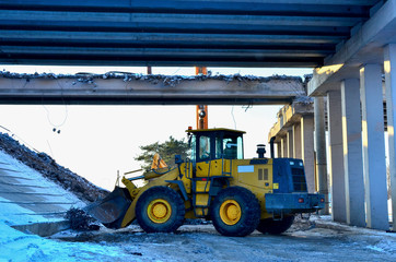 Front-end loader  on a construction site. Diesel bulldozer with a bucket. Work on the dismantling of reinforced concrete slabs from the road bridge