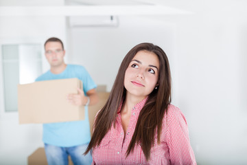 Portrait of beautiful, excited woman and man standing in front of the unpacking cardboard boxes in new home and looking up