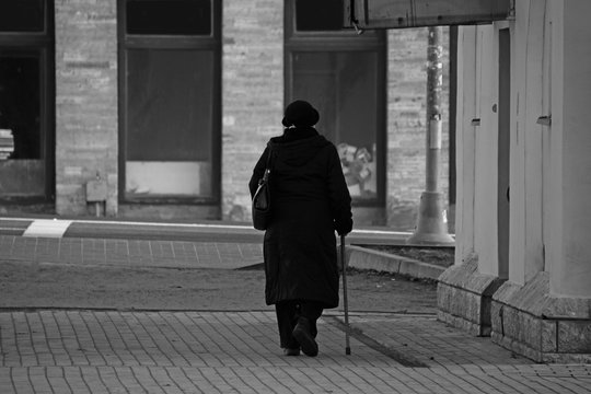 Black and white elderly woman with a stick walking down the street