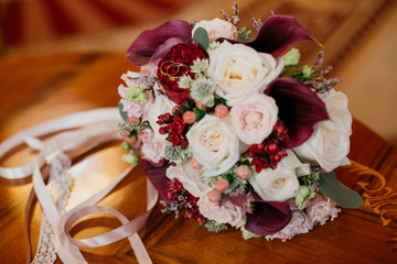  bridal bouquet with ribbons of roses, peonies and claret callas on the table. with wedding rings.