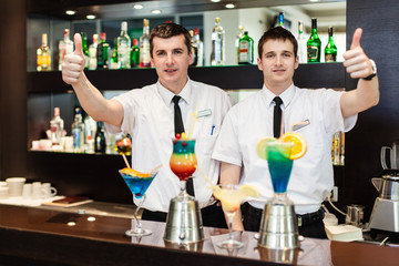 Two bartenders prepares beautiful cocktails. Authentic atmosphere and light