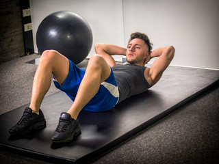 Attractive muscular young man in gym working out, doing exercises for abs on the ground