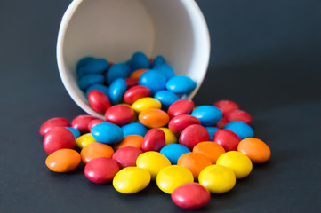 multicolored round dragee candies poured from an inverted paper cup on a black background