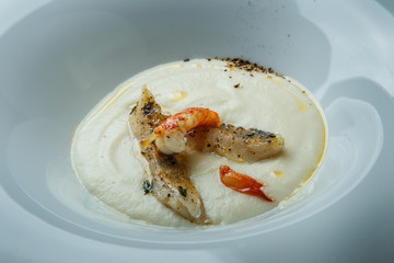 closeup fresh fish cream soup decorated with fried pieces of fish, prawn, and spices