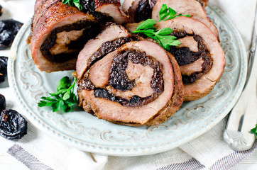 Baked turkey roll with prunes on a plate on a white wooden table