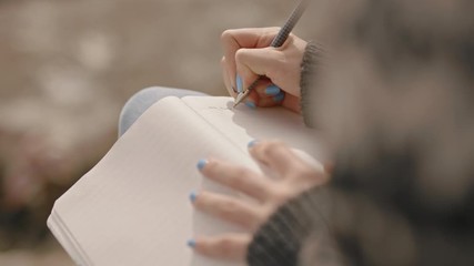 close up hands woman writing in diary journal teenage girl expressing lonely thoughts on seaside beach - Powered by Adobe