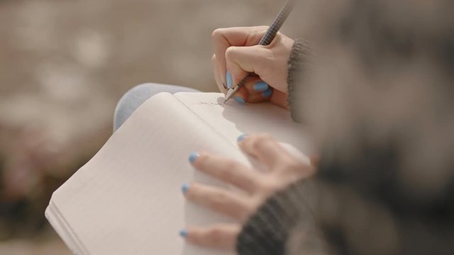 close up hands woman writing in diary journal teenage girl expressing lonely thoughts on seaside beach 