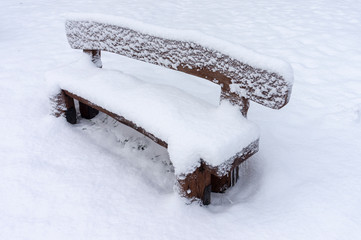 Snow-covered rustic wooden bench in a winter park