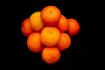 Pile of fresh orange mandarines forming a pyramid strongly contrasting on a black background