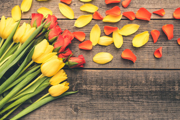 A bouquet beautiful tulips and roses arranged on an old, natural boards. Composition with yellow and red plants with flowers petals. Romantic frame with free, copy space. Wedding or valentine day.