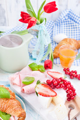 Sweet spring breakfast with croissants and bacon on a light background. A bouquet of red tulips and fresh berries of strawberries and currants. The concept of holiday celebration.