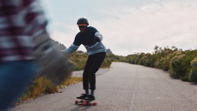 young friends longboarding together enjoying relaxed summer vacation riding skateboard on road teenagers cruising in countryside wearing protective helmet