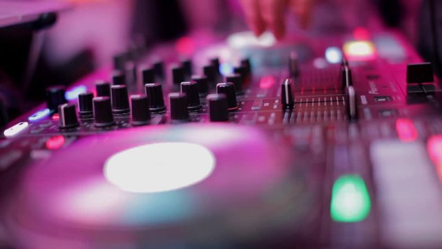 Close-Up of Dj Mixer Controller Desk in Night Club Disco Party. DJ Hands touching Buttons and Sliders Playing Electronic Music