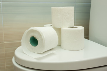 Several rolls of toilet paper are on the toilet lid