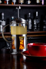 Sea buckthorn tea in french press on a bar background at coffee shop.