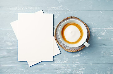 Obraz na płótnie Canvas Cup of latte coffee and white paper cards on painted wooden background
