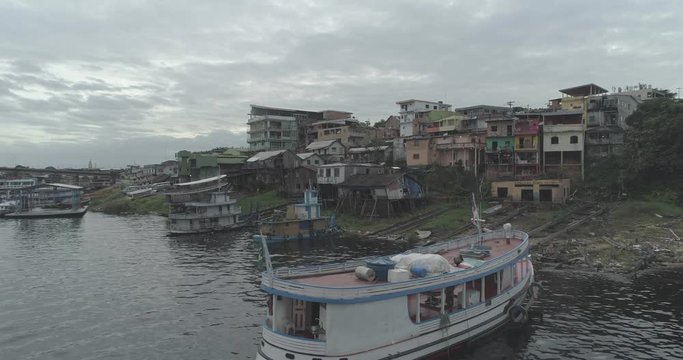 Low aerial rising up over painted wooden river boat on the Amazon River to dense poor housing in Manaus, Brazil