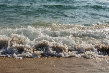 Foamy sea waves on the sandy beach with a soft light before sunset